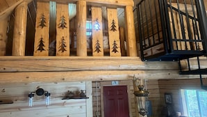 A wooden interior with a loft area featuring a railing with tree cutouts, a red door, and a lantern. - Cowboy Cabin -tucked into the woods near Hatcher Pass Recreation Area. (Palmer)