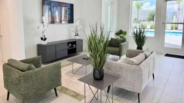 A spacious living room with a grey sofa set, a coffee table, and a large window offering a view of a swimming pool.
