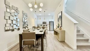 A modern dining area with a long table, chairs, and a contemporary light fixture.