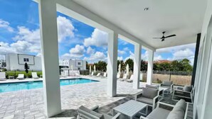 A covered outdoor area with a pool, lounge chairs, and a ceiling fan.