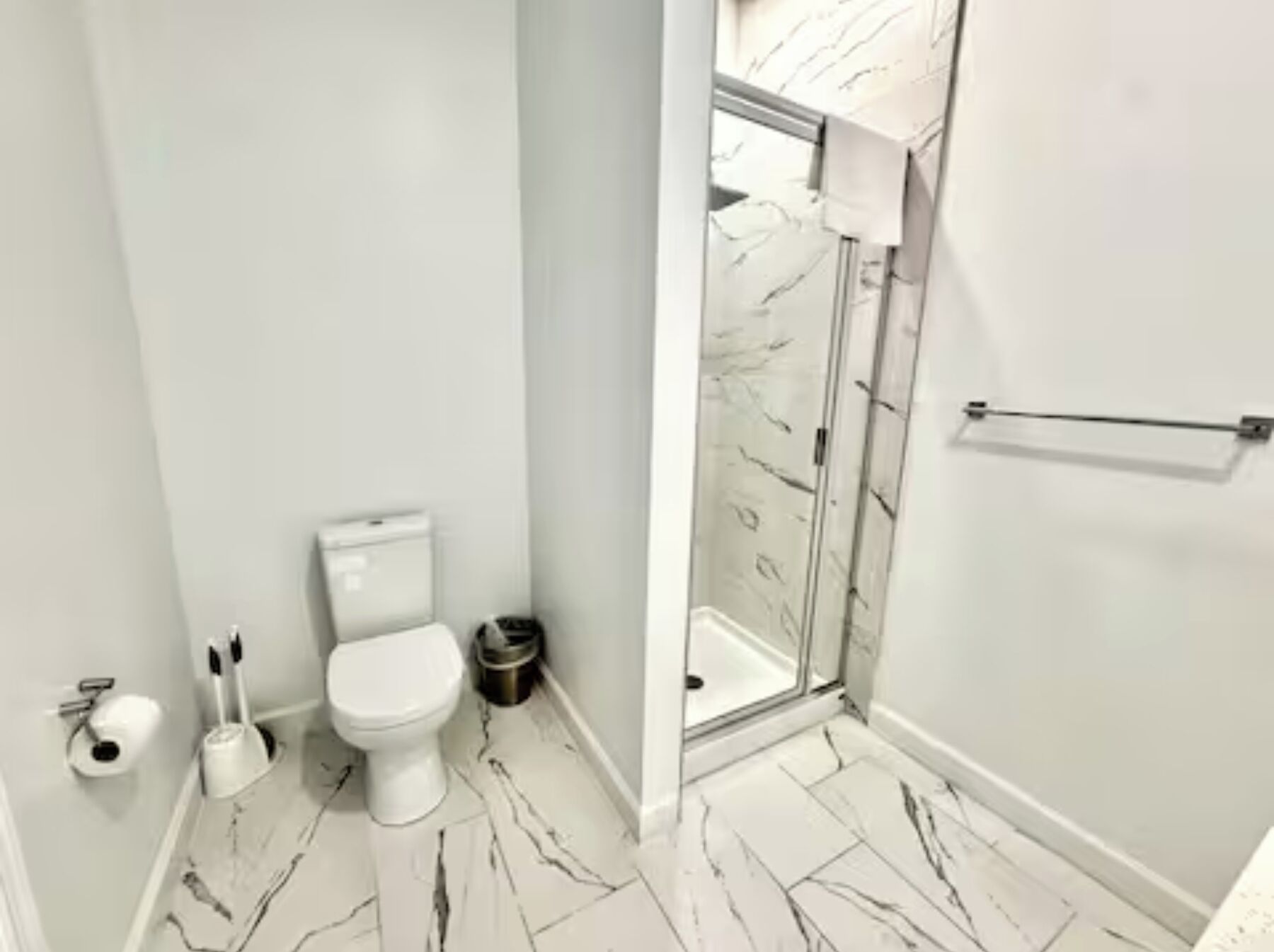 Un baño con inodoro, un cubo de basura y zona de ducha con puerta de cristal.