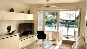 A modern living room with a sofa, a coffee table, and a TV. There is a kitchen area with cabinets and a countertop. - T2 apartment plus cabin with terrace and pool (Bormes-les-Mimosas)