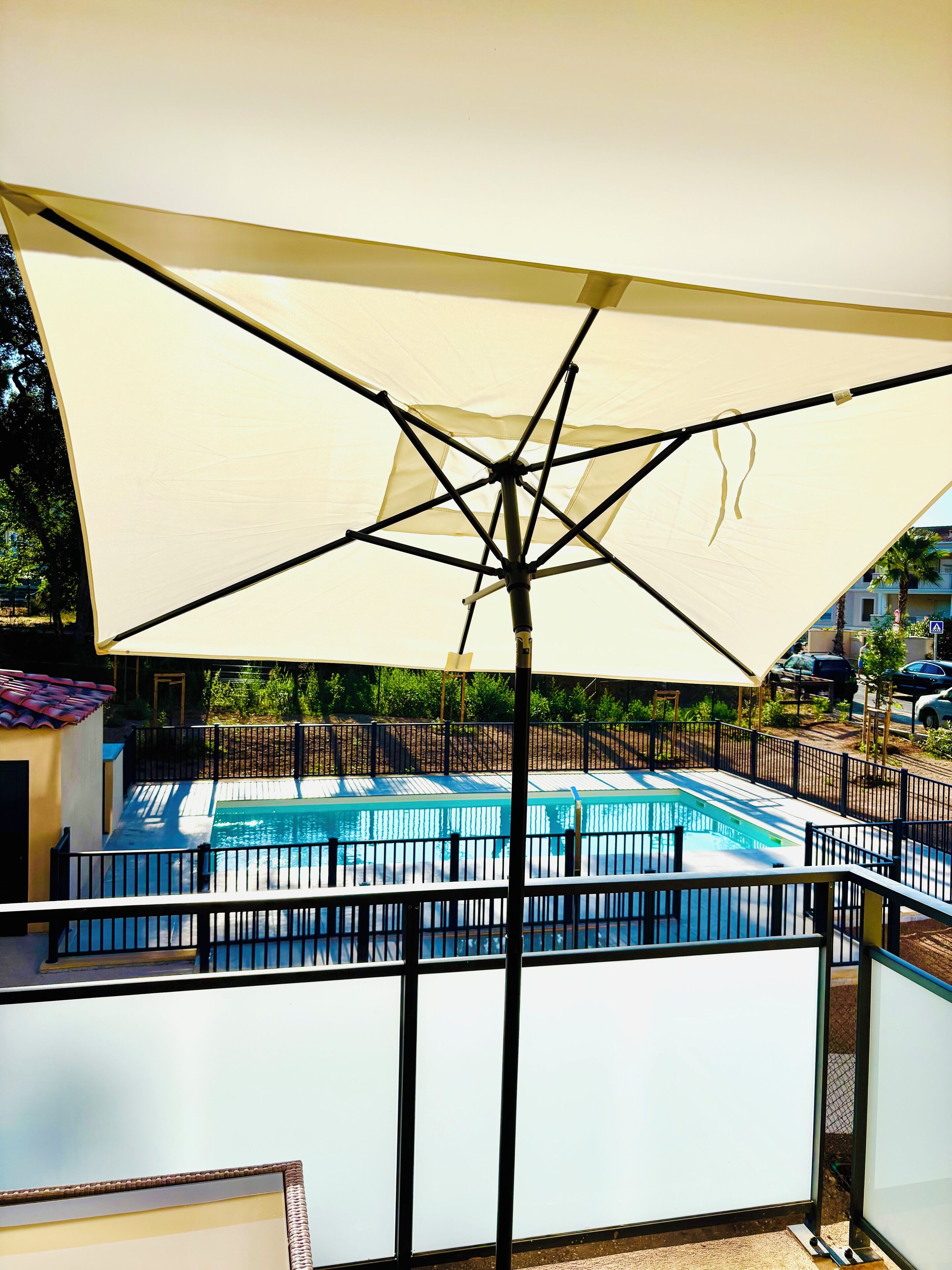 Área da piscina com um grande guarda-sol, piscina cercada e vista dos arredores.