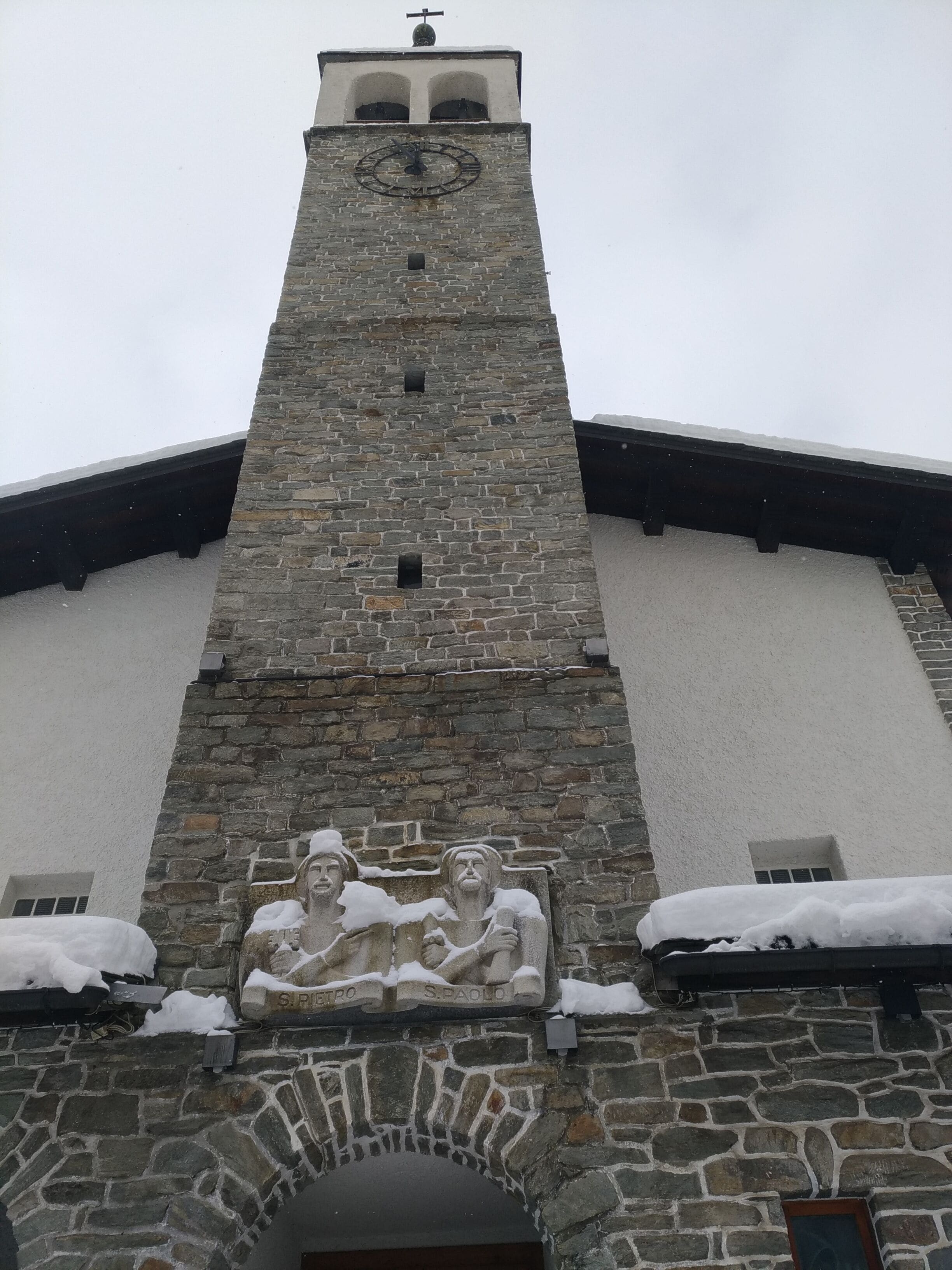 A stone tower with a clock and a relief sculpture of two figures.