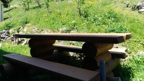 A rustic picnic table set in a grassy area with a backdrop of trees and a hill.