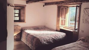 A room with two beds, wooden beams on the ceiling, a window with curtains, and a small table.