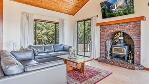 Een woonkamer met een grijze leren bank, een houten salontafel en een open haard van baksteen.