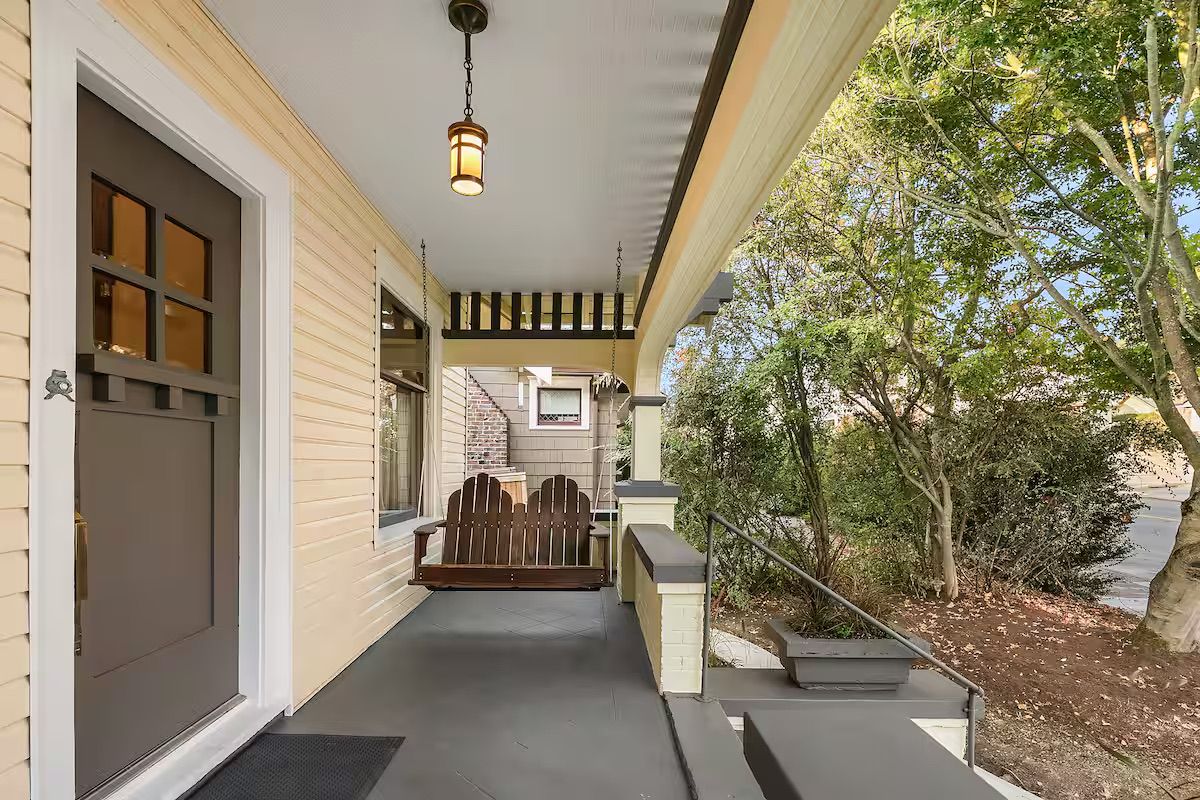 A covered porch with a wooden bench, a garage door, and a hanging light fixture.
