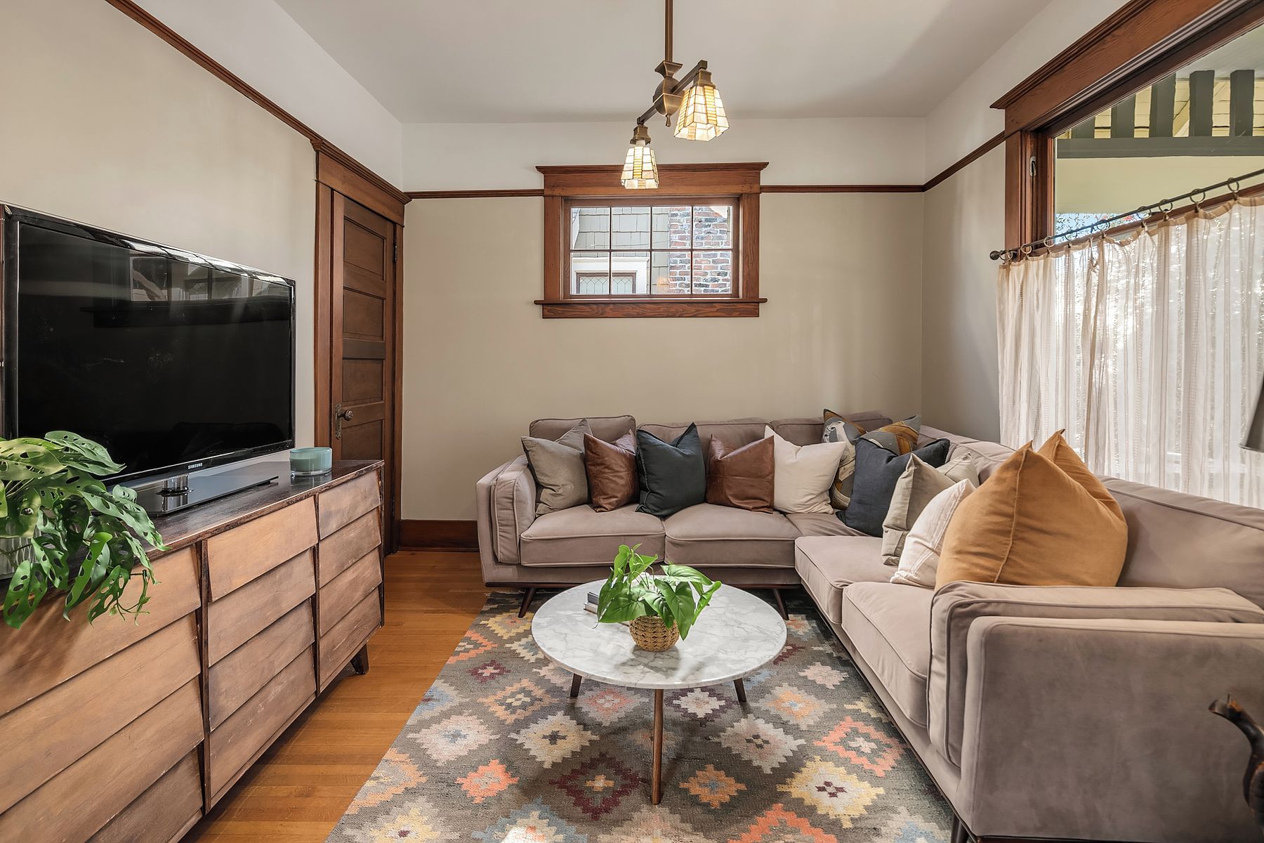 A living room with a sofa, a coffee table, a TV, and a window with curtains.
