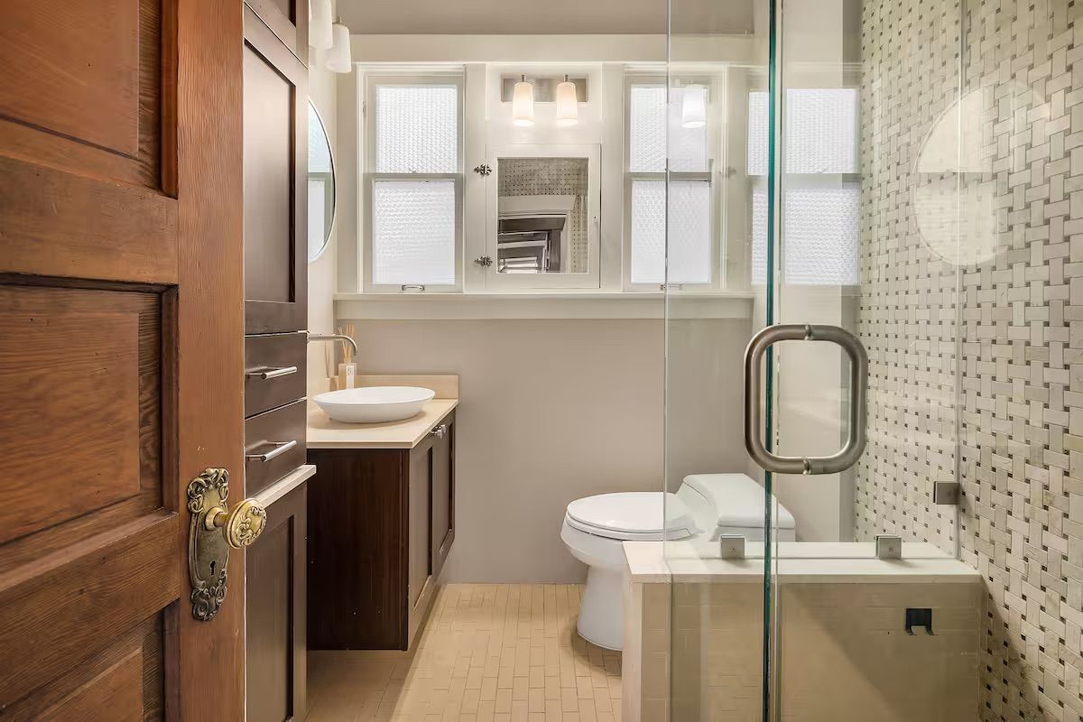A modern bathroom with a wooden door, a white sink, a toilet, and a glass shower enclosure.