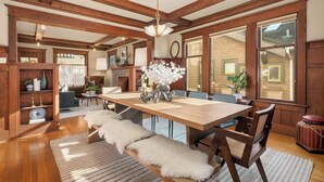 A spacious dining area with a wooden table and benches, surrounded by large windows and a brick wall. - Refined Wallingford Craftsman • Perfect Family Retreat near Parks, Zoo & UW (Seattle)