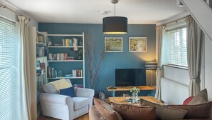 A living room with a sofa, a chair, a wooden coffee table, a bookshelf, a flat-screen TV, and a window with curtains.