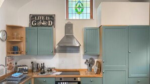 A kitchen with teal cabinets, a stainless steel range hood, a toaster, and a clock on the wall.