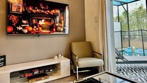 Sala de estar com televisão de tela plana na parede, um sofá e porta de vidro que dá para uma área externa.