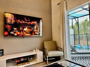 A living room with a flat-screen TV mounted on the wall, a sofa, and a glass door leading to an outdoor area. - The Fantasy Retreat4 by Disney/Universal/seaworld (Davenport)