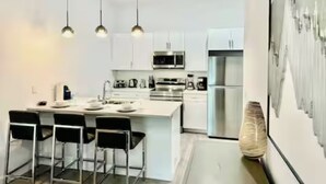 Uma cozinha moderna com armários brancos, eletrodomésticos de aço inoxidável e banquetas pretas.