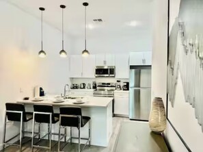A modern kitchen with white cabinetry, stainless steel appliances, and black bar stools. - The Fantasy Retreat4 by Disney/Universal/seaworld (Davenport)