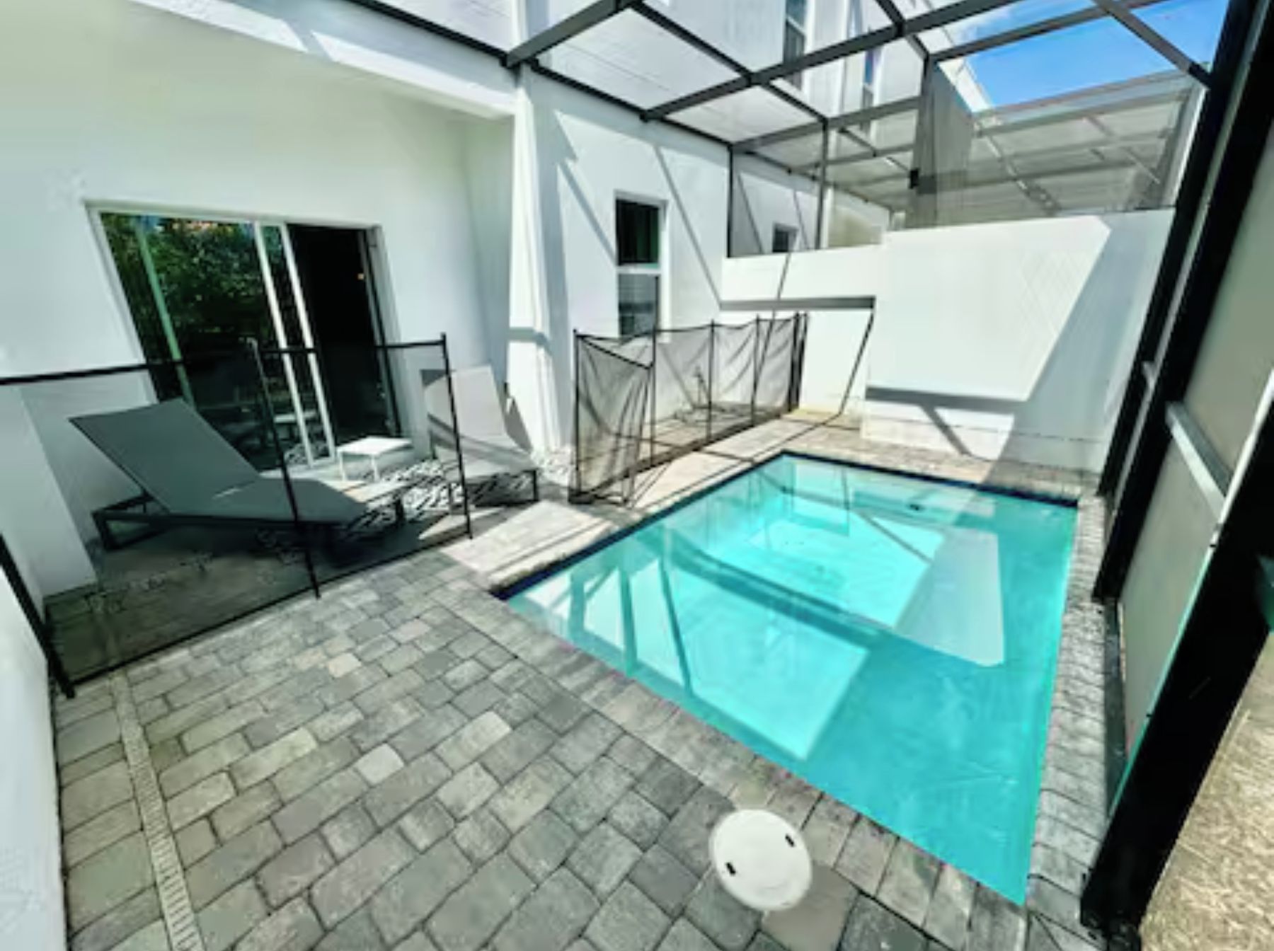 A modern outdoor pool area with a clear blue pool, a glass-enclosed lounge area, and a paved patio.