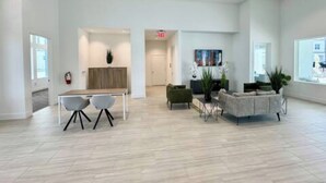Um hall amplo e moderno, com piso claro, balcão de recepção e áreas de estar com cadeiras e um sofá.