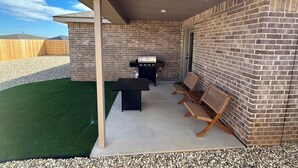 A covered patio area with a brick wall, a grill, and two wicker chairs.
