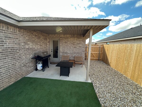 Une terrasse avec un barbecue, une table et des chaises, entourée d’un mur de briques et d’une clôture en bois.