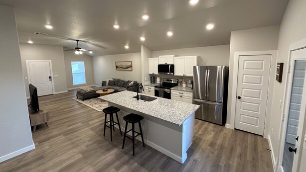 A modern kitchen with a central island, stainless steel appliances, and a dining area with a sofa and ottoman.