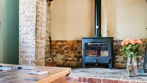 A rustic room with a brick wall, a wooden table, a black stove, and a vase with flowers. - 4 bedroom accommodation in Frogham, Fordingbridge (Frogham, Fordingbridge)