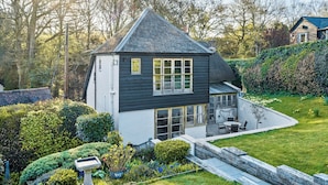A two-story house with a sloped roof, a front porch with seating, and a well-maintained garden. - 4 bedroom accommodation in Frogham, Fordingbridge (Frogham, Fordingbridge)