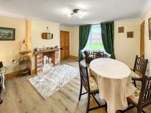 Un comedor con una mesa redonda, sillas, chimenea y vistas a través del ventanal.