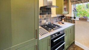 Una cocina con gabinetes verdes, estufa a gas y salpicadero de azulejos.