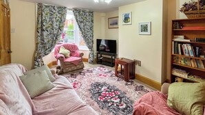 Una sala de estar con un sofá, una silla, un televisor, una estantería y una alfombra estampada.