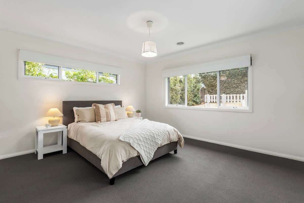 A bedroom with a bed, bedside tables, a lamp, and a window with a view of greenery and buildings.