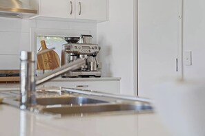 Eine Küche mit weißen Schränken, einer Edelstahl-Espressomaschine und einem Holztisch.