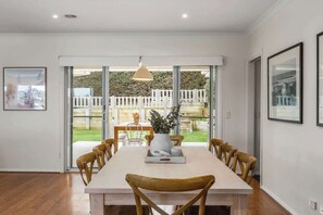 A dining area with a long table, wooden chairs, and a white vase with flowers.