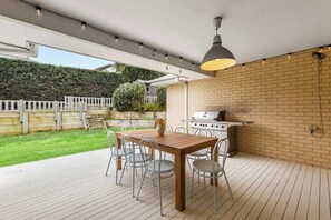 A patio with a wooden table and chairs, a grill, and a white fence.