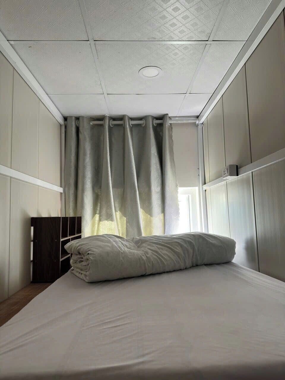 A single bed with a white mattress and pillow, a wooden headboard, and a ceiling with a recessed light fixture.