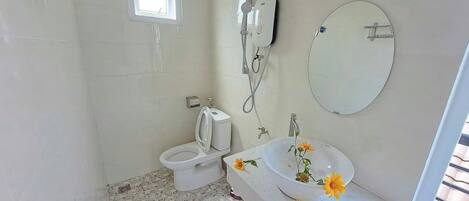 A bathroom with a toilet, a shower, and a sink with a mirror.