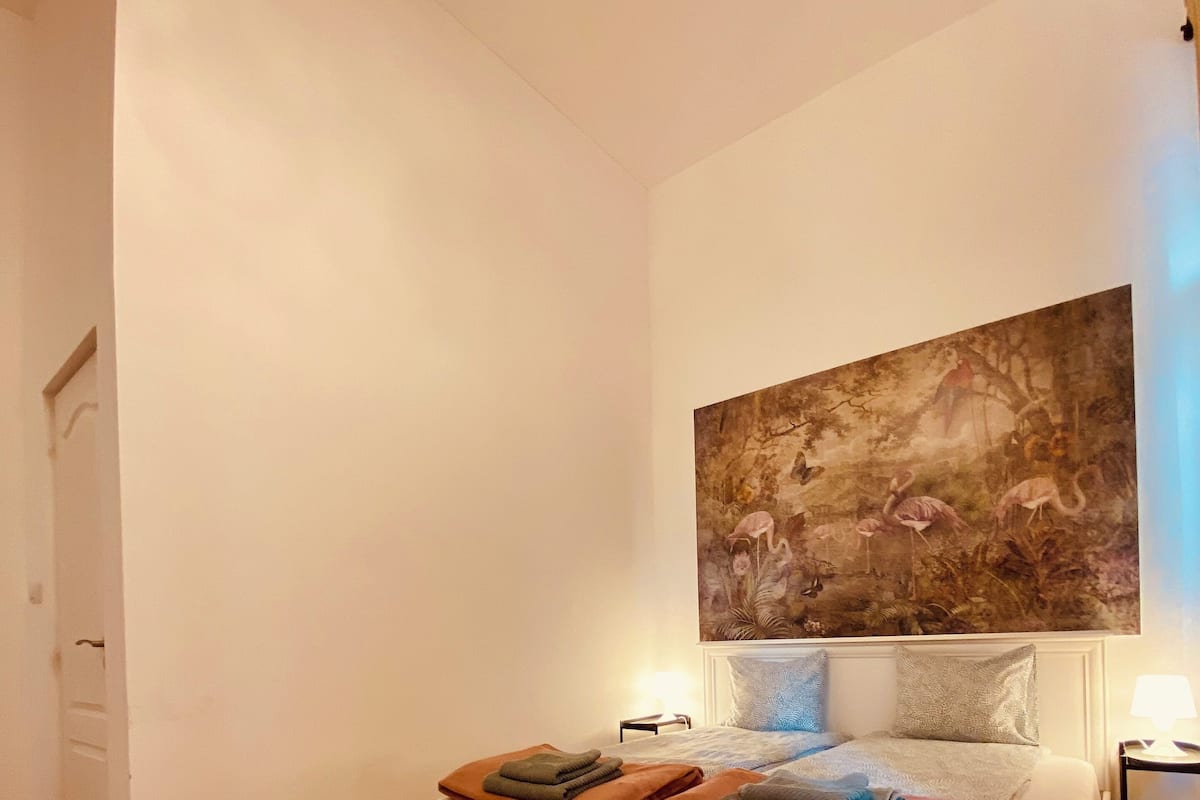 A bedroom with a bed, a painting on the wall, and a wooden floor.