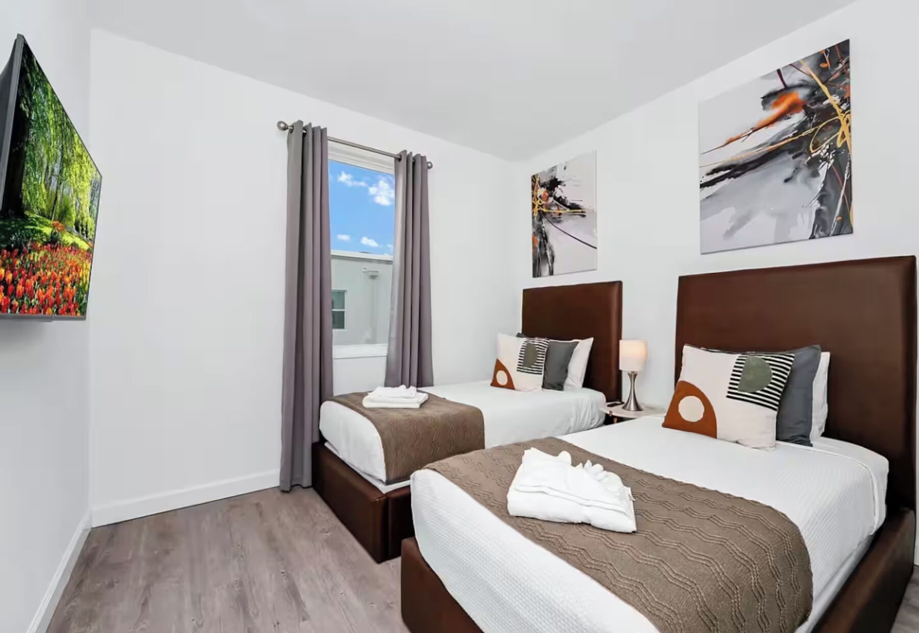 Ein Hotelzimmer mit zwei Betten, einem fenster mit Vorhängen, einem Bild an der Wand und Blick auf den Himmel.