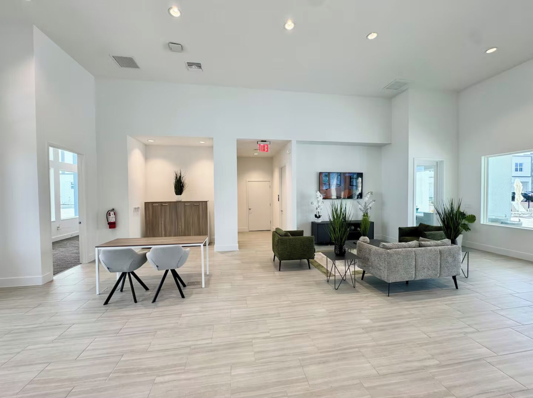 Un hall d’entrée spacieux et bien éclairé, doté d’un design moderne, comprenant un coin salon avec un canapé et des fauteuils, une petite table et un téléviseur fixé au mur.