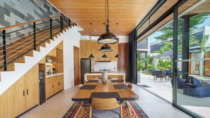 A modern kitchen with a wooden staircase, a dining area with a large table, and a view of the outdoors. - Sophisticated 3-Bedroom Designer Pool Villa in Central Seminyak (Badung)