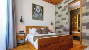 A modern bedroom with a wooden bed, a nightstand, a bedside table, a wall-mounted artwork, and a built-in shelving unit. - Sophisticated 3-Bedroom Designer Pool Villa in Central Seminyak (Badung)