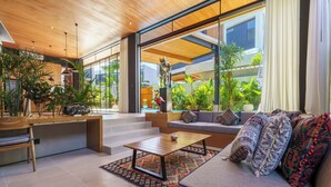 A modern living room with a sofa, coffee table, and a dining area with chairs and a table. - Sophisticated 3-Bedroom Designer Pool Villa in Central Seminyak (Badung)