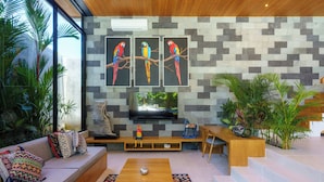 A modern living room with a sofa, coffee table, and TV. There are three paintings of parrots on the wall. - Sophisticated 3-Bedroom Designer Pool Villa in Central Seminyak (Badung)