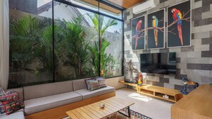A modern living room with a large window, a sofa, a coffee table, and a TV. - Sophisticated 3-Bedroom Designer Pool Villa in Central Seminyak (Badung)