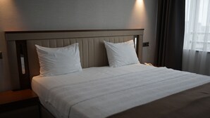 A neatly made bed with a headboard, a bedside table, and a window with curtains. - WEEN OTEL (Trabzon)