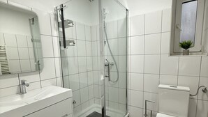 A modern bathroom with a glass-enclosed shower, white fixtures, and a small window. - City apartment - central with beautiful terrace (Herne)