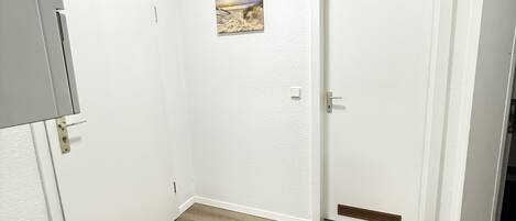 A room with a wooden floor, white walls, a door with a vent, and a small picture on the wall.