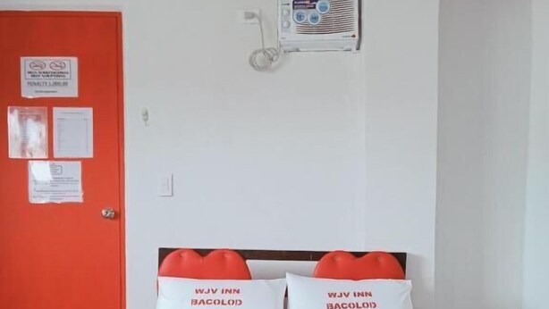 A hotel room with a bed, a red door, and a wall-mounted air conditioning unit.
