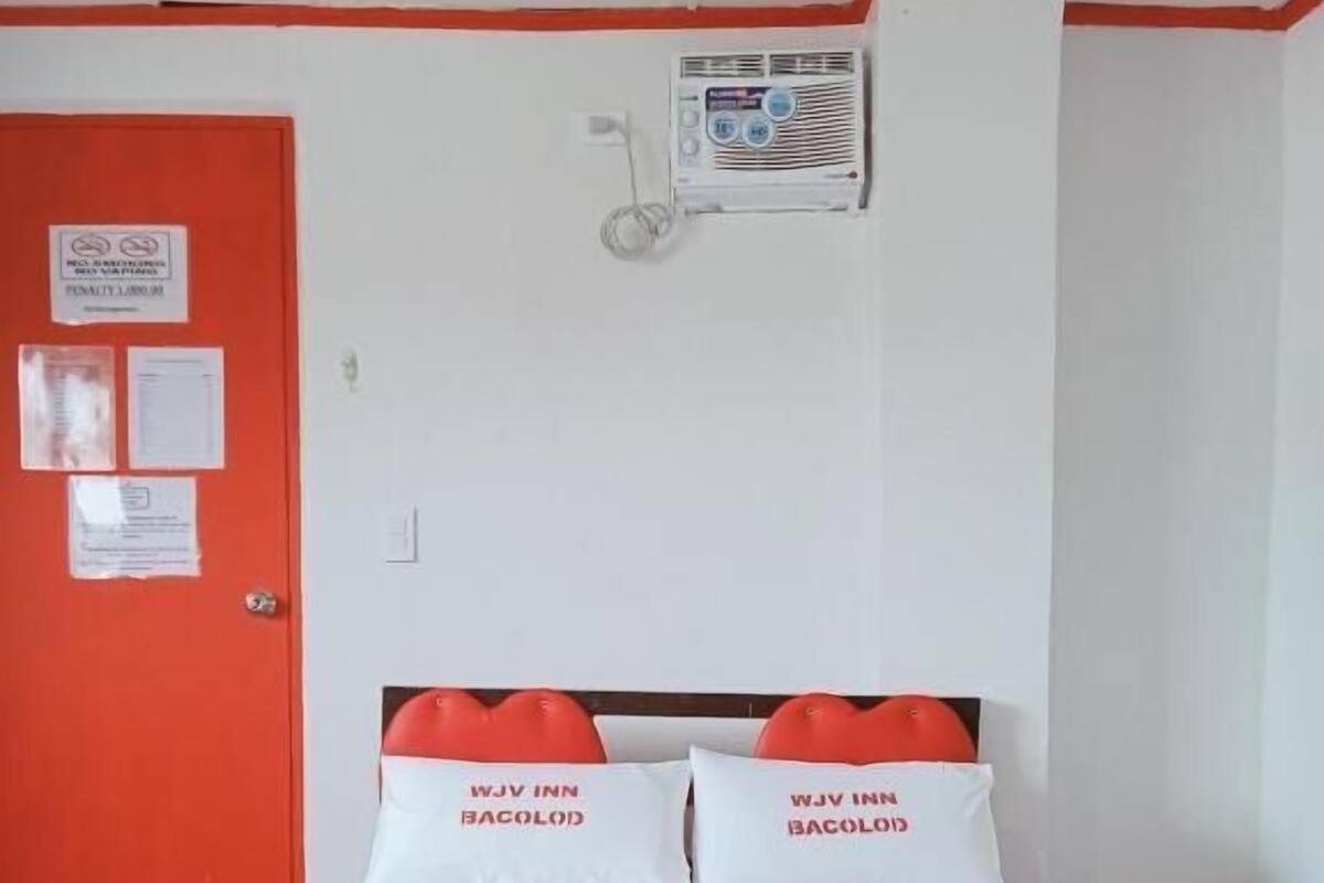 A hotel room with a bed, a red door, and a wall-mounted air conditioning unit.